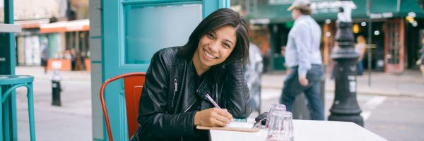 girl with notebook sitting at street cafe table