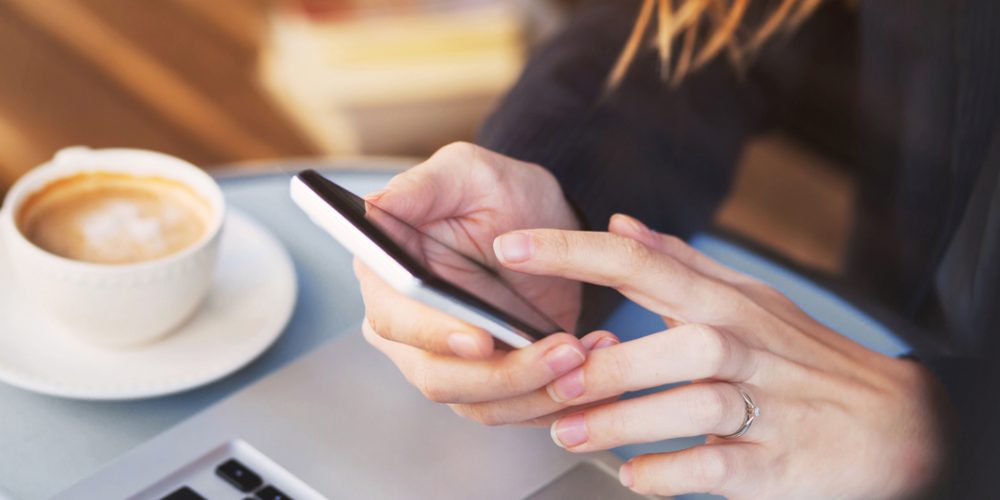 woman texting on smart phone with coffee nearby